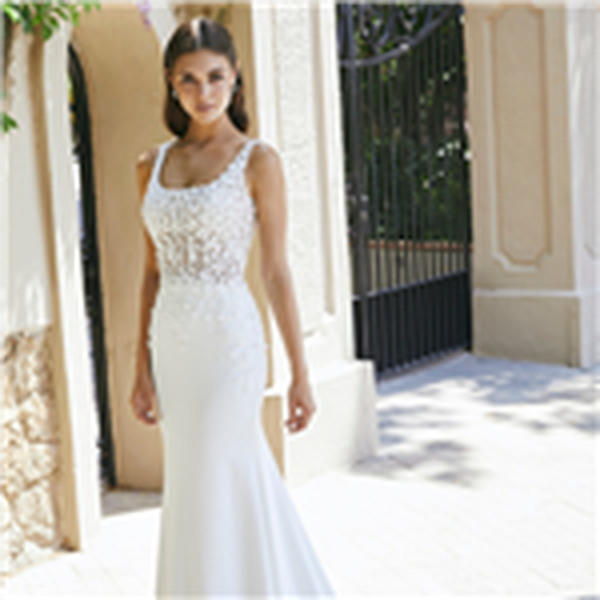 Brunette model stood in a sunny gated drive in Ronald Joyce 69702, a classic fit and flare wedding dress style with a scoop neckline, feminine 3D floral bodice and plain skirt.